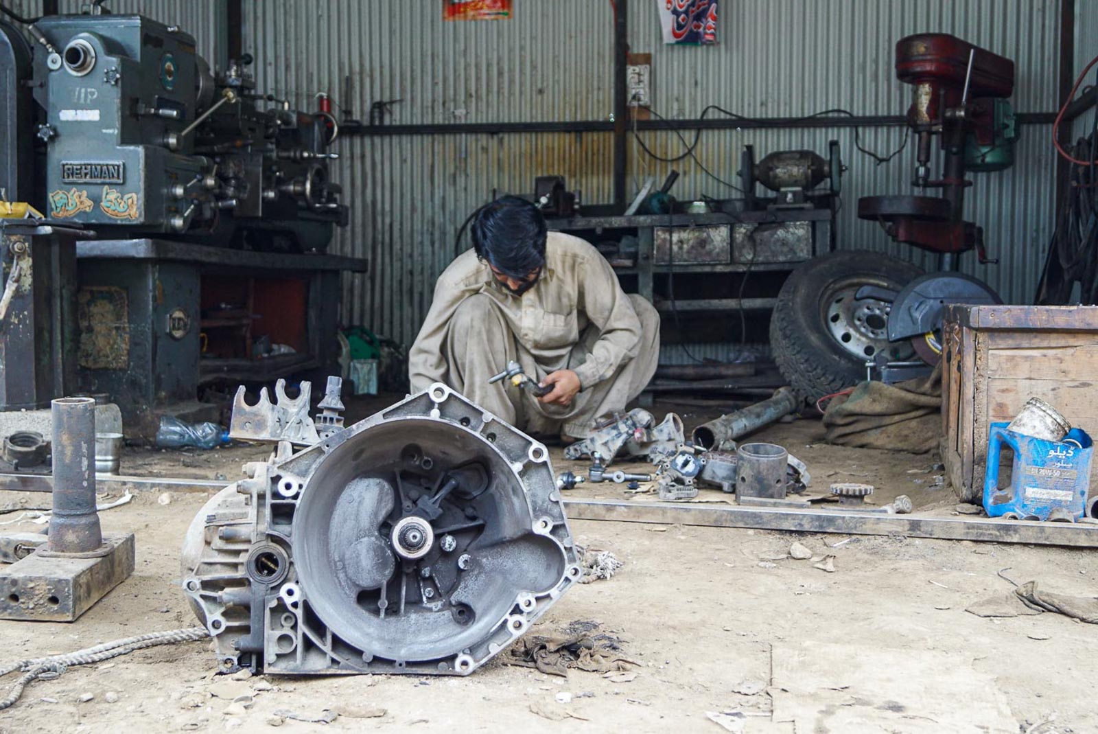 Pakistan in Naran, arbeitet ein Mechaniker am Getriebe. Man sitz in hockend in seiner kleinen Werkstatt. Er hat ein Beiges traditionelle Pakistanische Gewand an und schwarzes Haar
