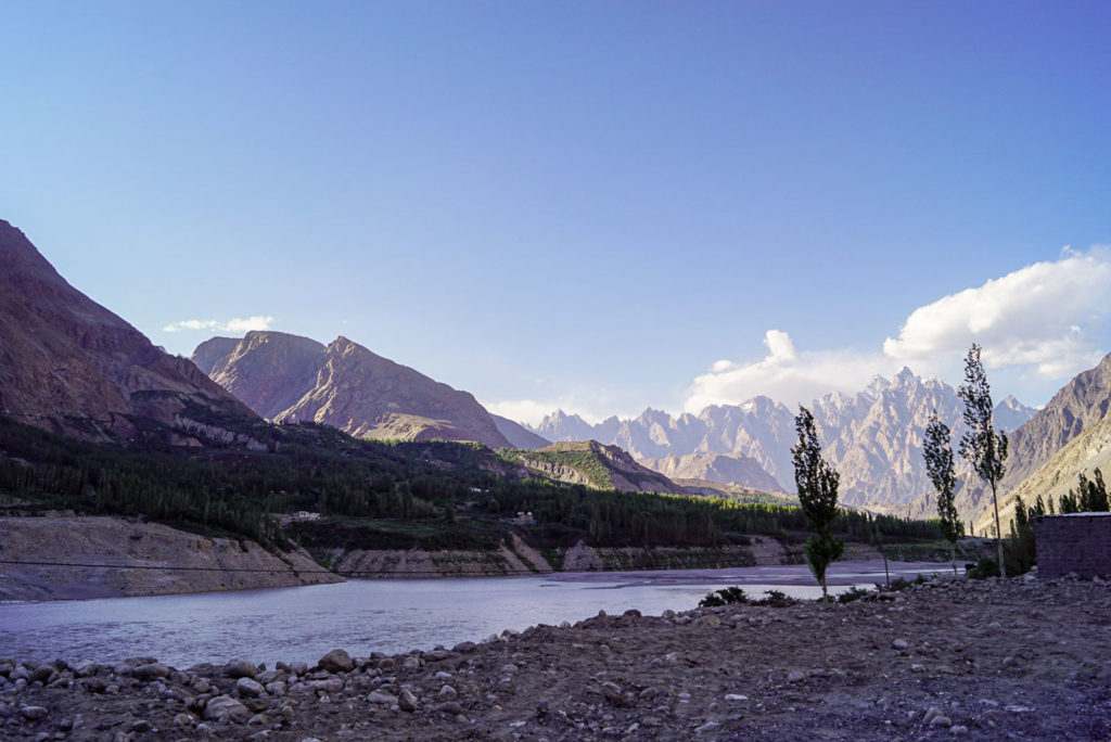 Berge und Fluss im Karakorum in Pakistan. Hellblauer Hintergrund udn schmale Bäume, gewässer die sonne scheint. Steiniger Vordergrund, Natur pur