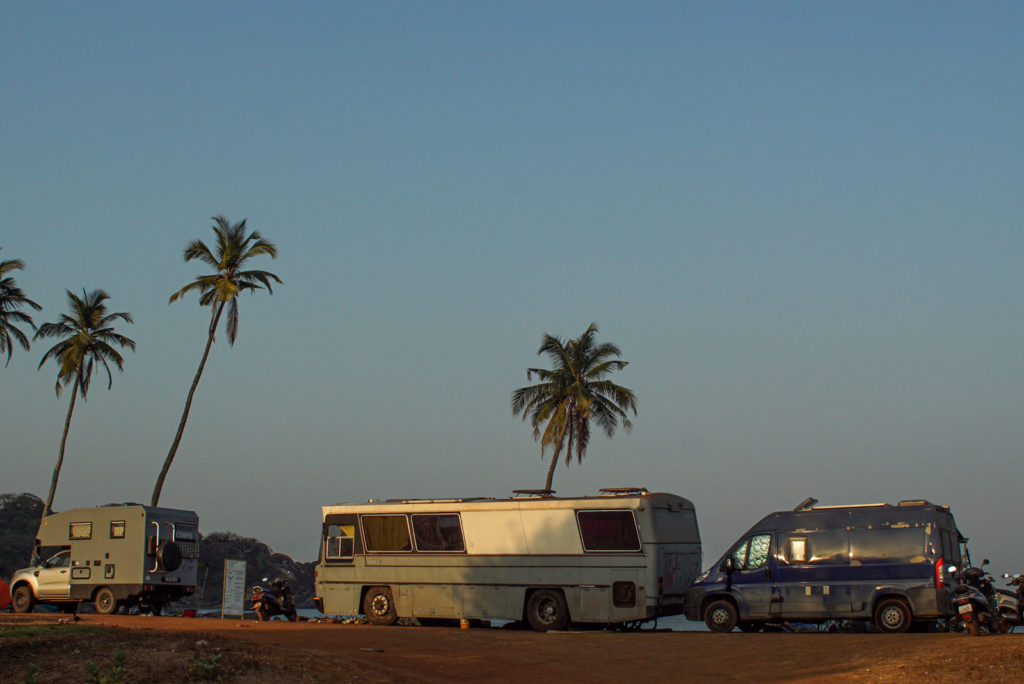 Auf dem Bild ist ein Strand in Indien, Goa, Agonda Beach mit Palmen zu sehen zusehen. AufIn der Linken Ecke steht ein Toyota mit Bi Mobil aufbau. In der Mitte erin alter grauer Mercedes Bus und Rechts unser blauer Fiat Ducato Kastenwagen.