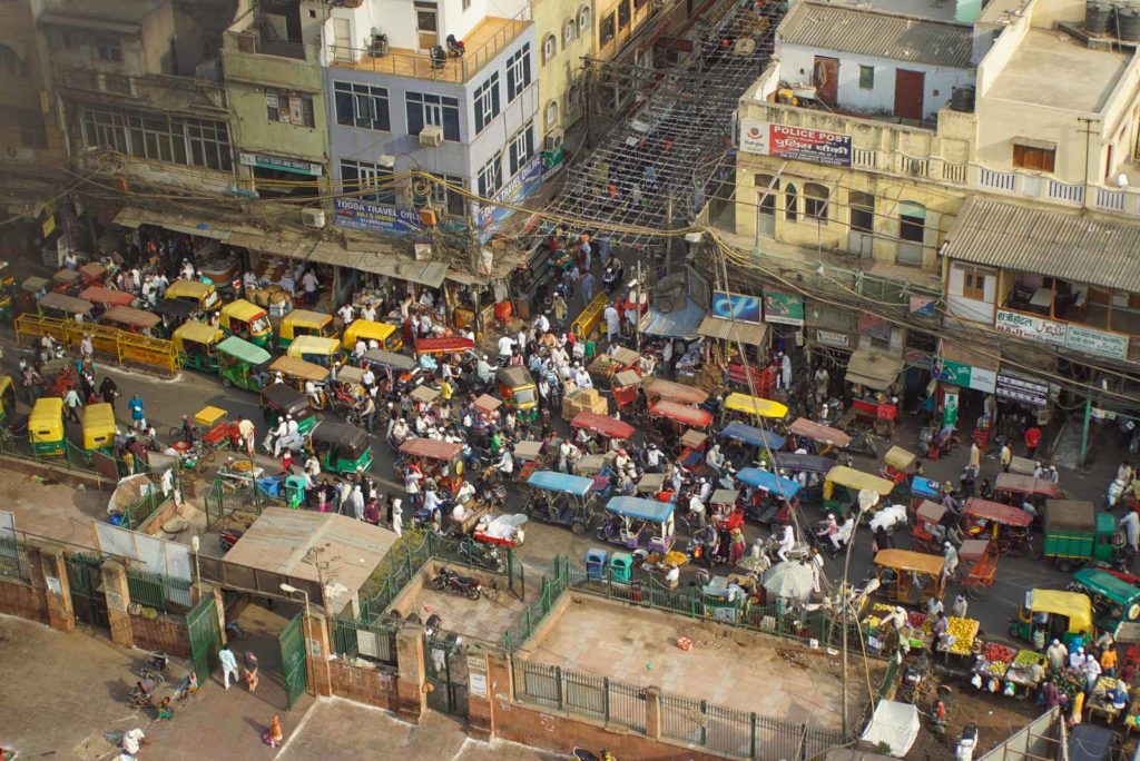 Zu sehen ist eine typische Straßenkreuzung in Indien. Rikschas, Motorräder und Fußgänger alle versuchen den kürzesten Weg zu nehmen und bringen den Verkehr damit zum erliegen.