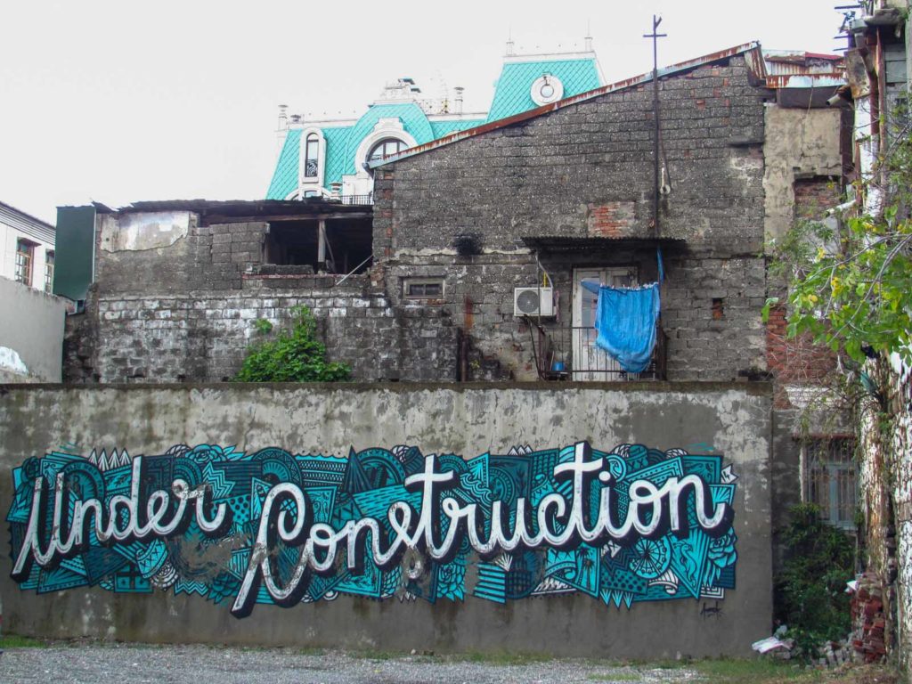 Haus in Georgien mit großer grauer Wand und großem Graffiti auf dem UNDER CONSTRUCTION steht